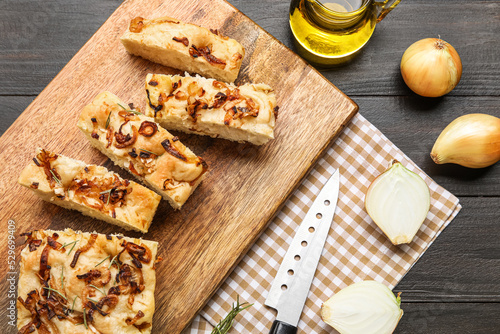 Board with tasty Italian focaccia and onion on dark wooden background, closeup