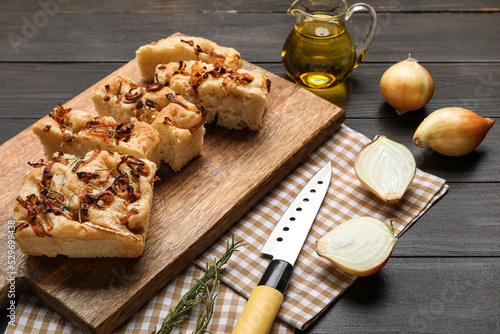 Board with tasty Italian focaccia and onion on dark wooden background