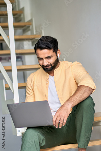 Indian man remote working on laptop device, using computer for virtual learning, surfing internet digital technology watching online web education webinar, having hybrid video call meeting from home. photo