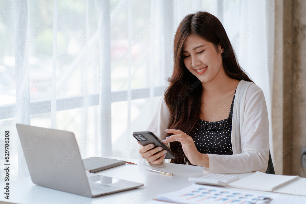 Happy young Asian businesswoman sitting on her workplace in the office. Young woman working at laptop computer in the office Happy young Asian businesswoman sitting on her workplace in the office. Young woman working at laptop computer in the office