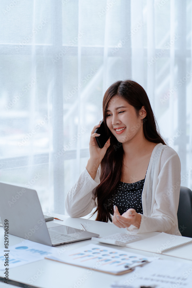 Happy young Asian businesswoman sitting on her workplace in the office. Young woman working at laptop computer in the office Happy young Asian businesswoman sitting on her workplace in the office. Young woman working at laptop computer in the office