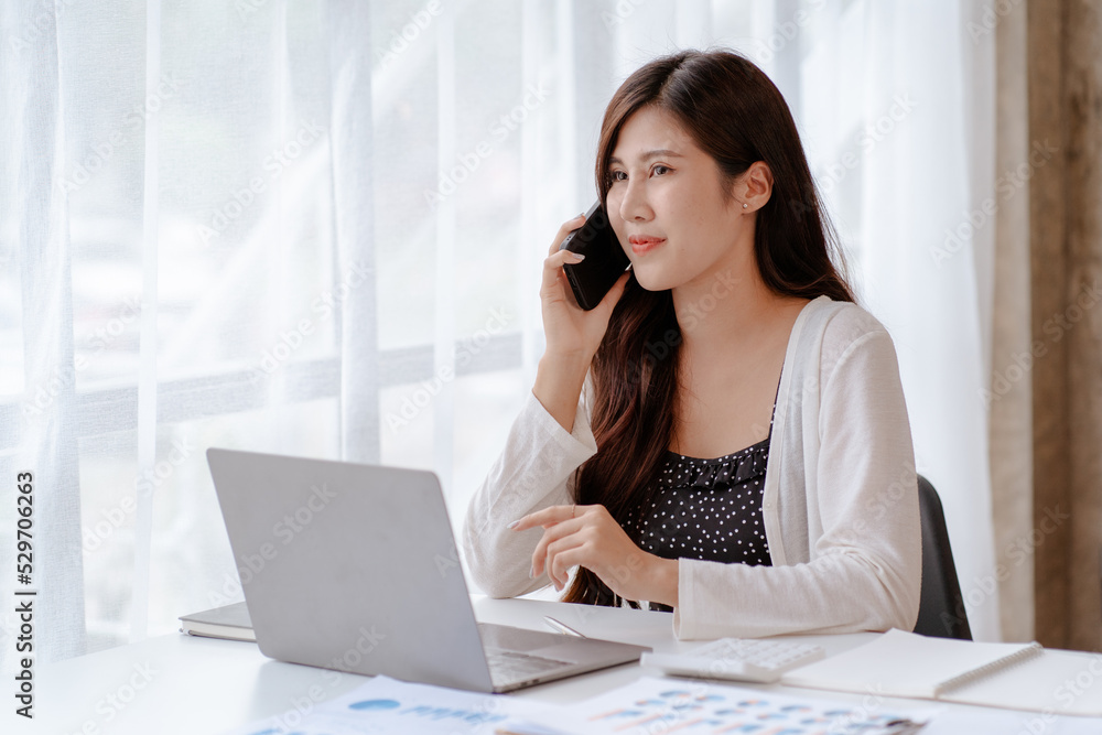 Happy young Asian businesswoman sitting on her workplace in the office. Young woman working at laptop computer in the office Happy young Asian businesswoman sitting on her workplace in the office. Young woman working at laptop computer in the office