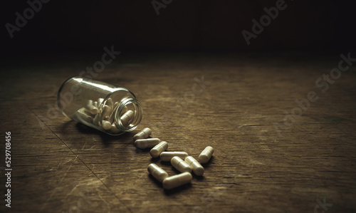 A glass bottle with white pills on a wooden table in vintage style. Old pills.