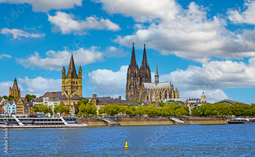 Cologne, Germany - July 9. 2022: Beautiful river rhine waterfront skyline, two churches, dom, cruise ships, blue summer sky fluffy white clouds