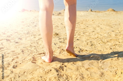 Summer concept: a beach with yellow sand and women's legs on a sunny summer day. Selective focus.