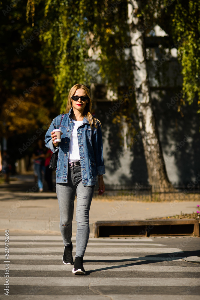 girl in a denim jacket with coffee in her hands crosses girl in a denim jacket with coffee in her hands crosses