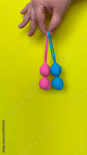 Sex toys. Two geisha balls on a hand. Yellow background. Useful for sex shop, adult
