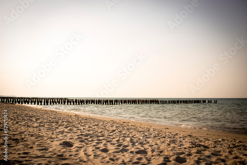 Plaża nad polskim morzem na tle zachodzącego słońca z falami i falochronem photo