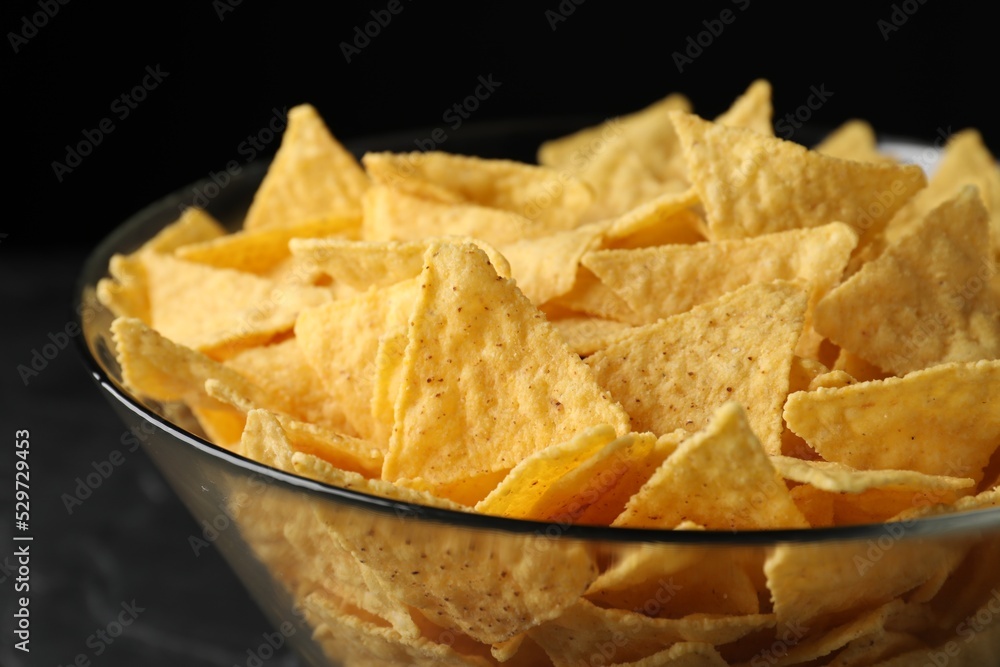 Glass bowl with tortilla chips (nachos) on black table, closeup Glass bowl with tortilla chips (nachos) on black table, closeup