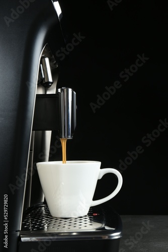 Modern espresso machine pouring coffee into cup on grey table against black background