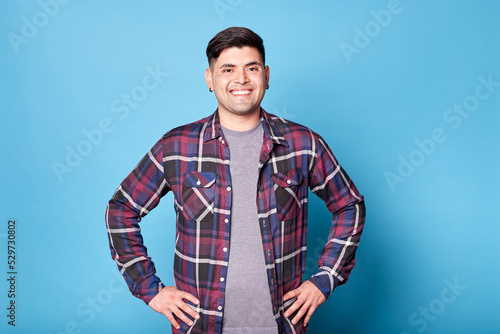 Portrait of a happy latino young man smiling looking at camera isolated on blue background. Copy space. © Lux Images