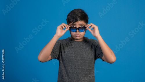 Retrato de estudio de un niño sonriente que se quita las gafas de sol sobre fondo azul.