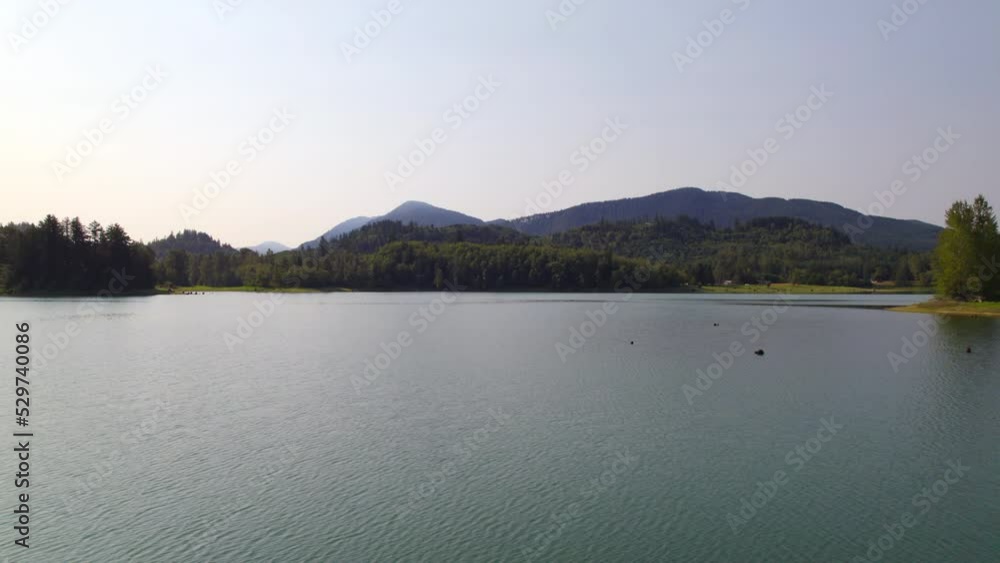 Trucking shot to the right of a miniture island cover with grass and trees in the reflective waters of Alder Lake on a hazy and sunny morning. Trucking shot to the right of a miniture island cover with grass and trees in the reflective waters of Alder Lake on a hazy and sunny morning.