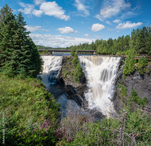 Kakabeka Falls, the second largest waterfall in Ontario (behind only Niagara Falls) plunges down a rocky cliff, as seen from a lookout point.