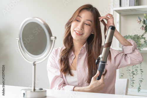 Fotobehang women hairdo makeup routine, Young woman looking at the mirror and using iron hair curling curly long hair at home