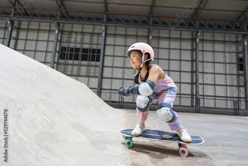 asian child skater or kid girl playing skateboard or riding surf skate up to wave ramp or wave bank to fun bottom turn and sweating in skate park by sports exercise to wearing helmet for body safety