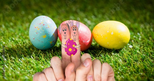 Close-up of cropped hands with bunnies drawing on index fingers against easter eggs on grass