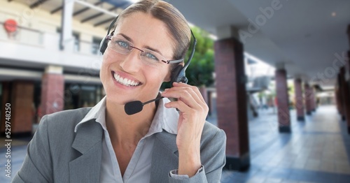 Composite image of caucasian businesswoman with phone headset smiling against corridor in background