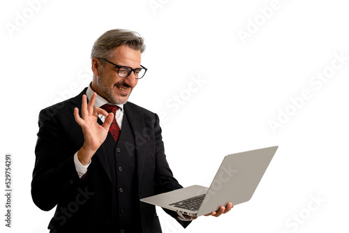 Portrait of Businessman in elegant blue suit wearing eye glasses looking at his laptop screen while holding his laptop and showing ok gesture. isolated on white background with copy space. © Jirus