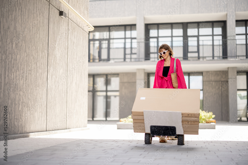 Woman carries furniture in boxes on a cart, delivering them home. Process of self improvement apartment, buying furniture and delivery