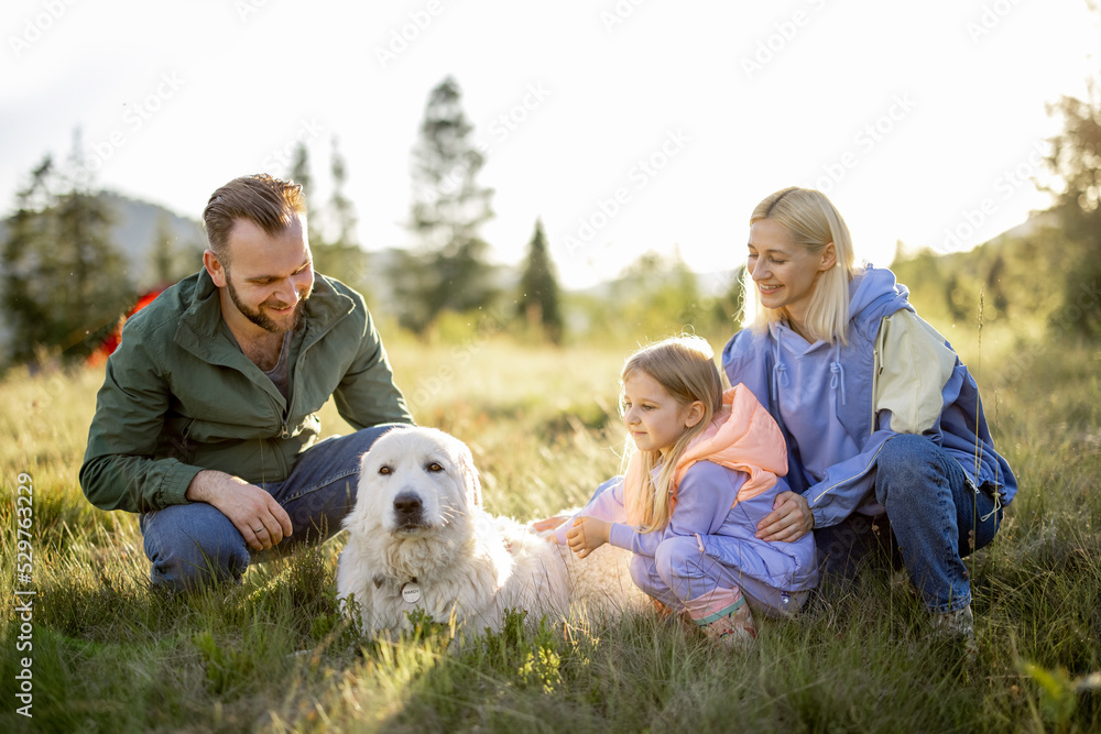 Portrait of a lovely couple with little girl and dog sit together while travel in the mountains. Young caucasian family spend summer vacation on nature Portrait of a lovely couple with little girl and dog sit together while travel in the mountains. Young caucasian family spend summer vacation on nature