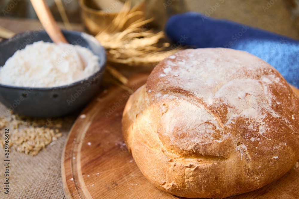 A loaf of fresh baked homemade whole grain sourdough bread, on a wooden board, bowl with flour and spikelets of wheat. A loaf of fresh baked homemade whole grain sourdough bread, on a wooden board, bowl with flour and spikelets of wheat.