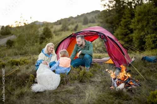 Young couple with a little girl have fun at campsite, traveling with tent on nature. Family spend summer time hiking in the mountains