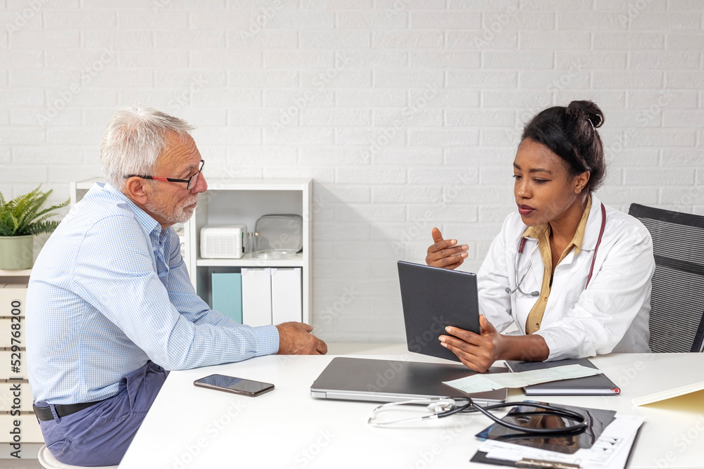 Afro american woman doctor using a digital tablet during a consultation with a senior man in ambulance with laptop on desk Afro american woman doctor using a digital tablet during a consultation with a senior man in ambulance with laptop on desk