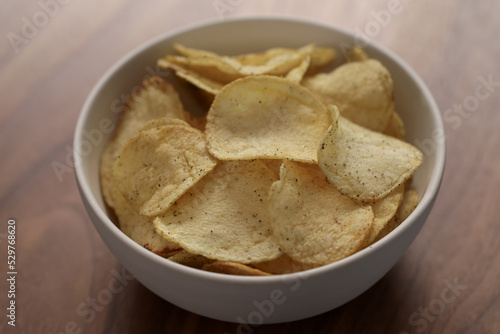 Organic potato chips with black pepper in white bowl on wood table