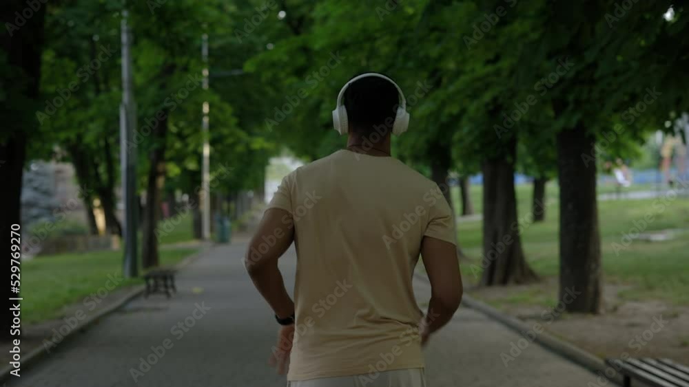 Back view of the afro american man running in the park wearing headphones. male athlete running enjoying their summer morning workout. Sport and healthy lifestyle concept. Back view of the afro american man running in the park wearing headphones. male athlete running enjoying their summer morning workout. Sport and healthy lifestyle concept.