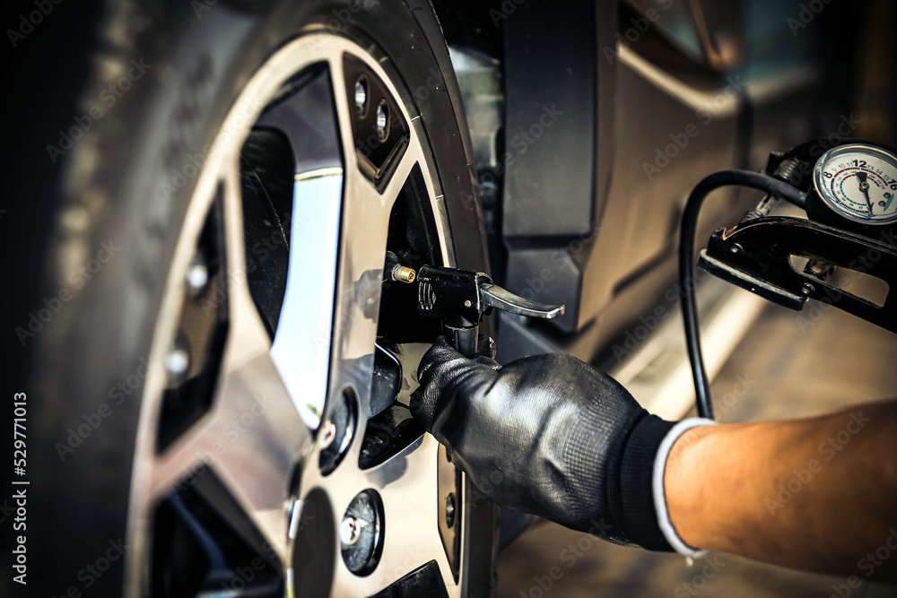 Fototapeta premium Auto mechanic checking air pressure and inflating car tires. Concept of car care service and maintenance or fix the car leaky or flat tire.