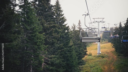The chair cable car in the mountains slowly moves up past the tall fir trees. photo