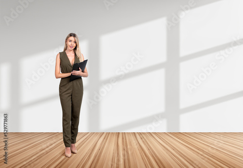 Businesswoman is standing holding clipboard near empty white wal