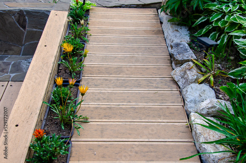 Walkways made of wood-plastic composite boards. A border made of natural stone and flower pots. Gardening and decoration of the house plot. Solar lights