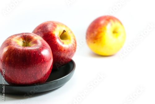 Red apples are placed on a black ceramic tray and rest on a white background.