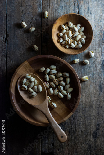 The pistachios are in a wooden tray with a wooden ladle. And in a wooden cup placed on a wooden table, top view.