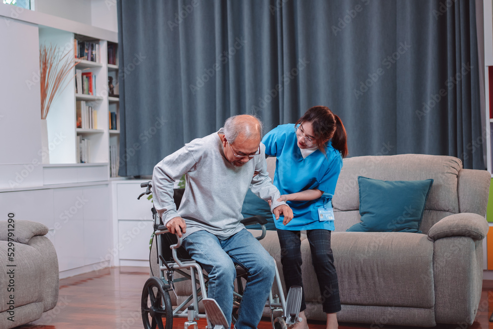 Asian senior elderly man patient doing physical therapy with caregiver. woman nurse helping get up from wheelchair for practice walking at home, practice walking slowly at nursing home care concept. Asian senior elderly man patient doing physical therapy with caregiver. woman nurse helping get up from wheelchair for practice walking at home, practice walking slowly at nursing home care concept.