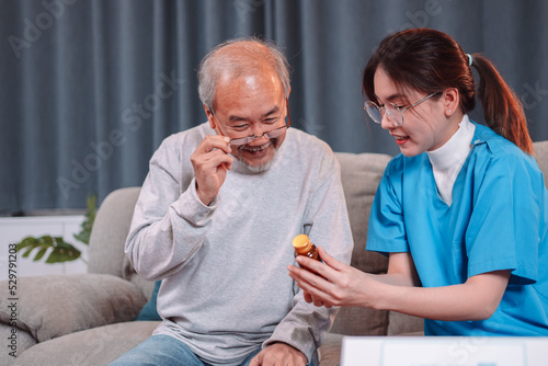Asian senior male patient consult prescription drug with physician nurse at nursing home. Caregiver therapist pharmacist woman hold medicine pills bottle, medicine dosage at house in living room.