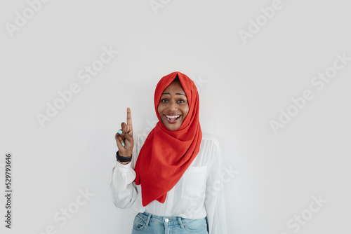Inspiration and eureka concept. Excited black muslim woman in hijab raising finger up and smiling, free space