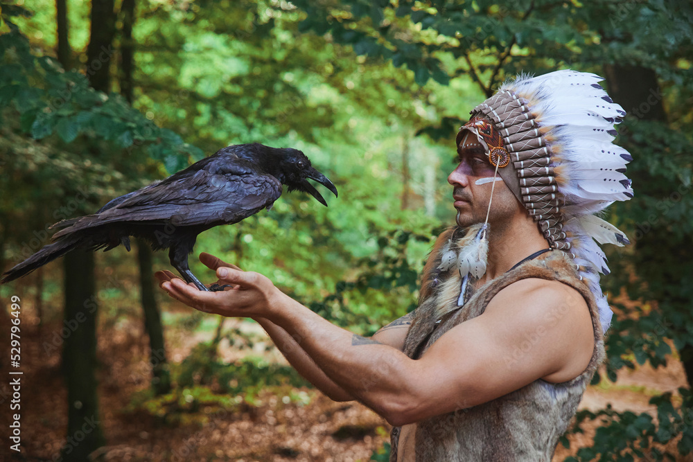 A man in traditional Native American clothing holding a crow 