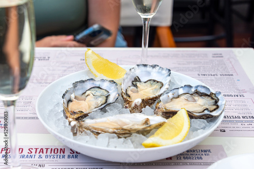 Opened oysters and lemon with white wine on the table. Restaurant delicacy, simple table setting. Saltwater oysters dish. Romantic dinner in restaurant