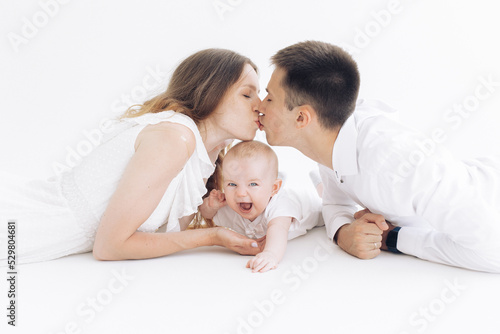 Happy parents lie and kiss each other next to their laughing son.
