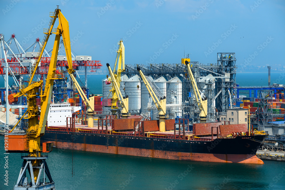 industrial seaport infrastructure, sea, cranes and dry cargo ship, grain silo, bulk carrier vessel and grain storage elevators, concept of sea cargo transportation