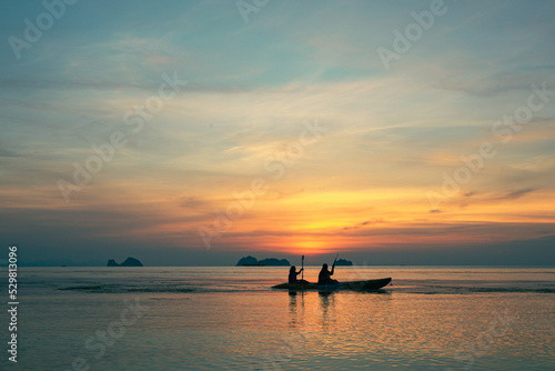 Silhouettes of a couple kayaking in the sea at sunset