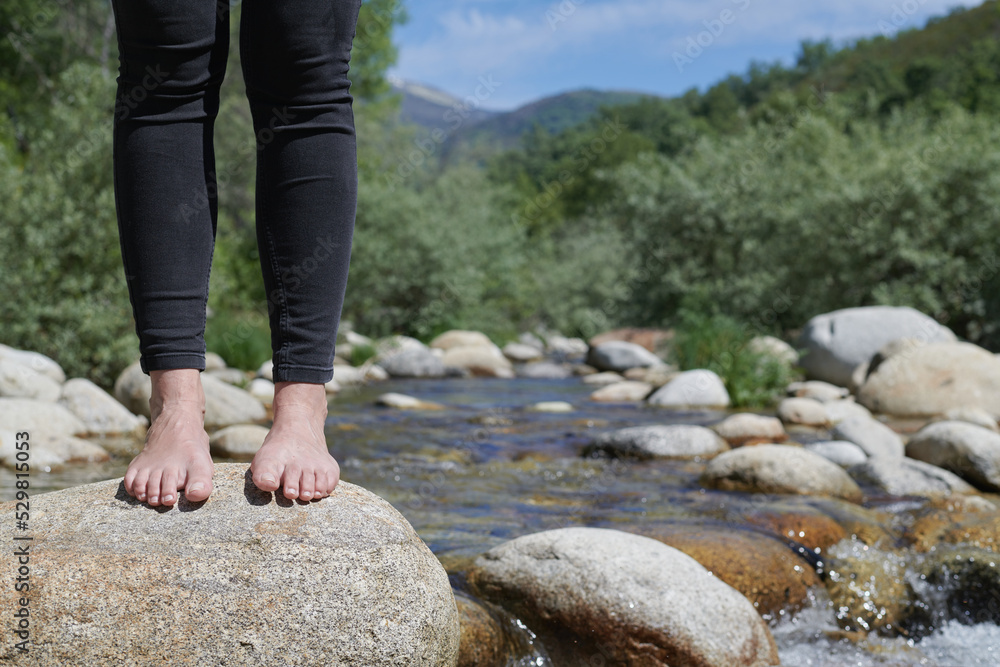 Barefoot young woman crossing river Barefoot young woman crossing river