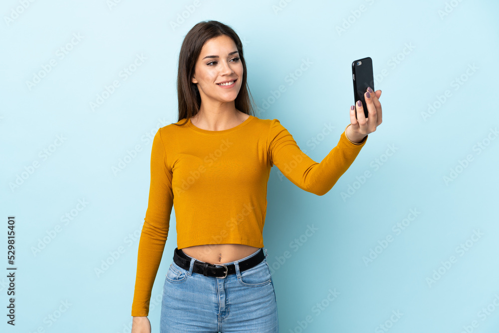 Young caucasian woman isolated on blue background making a selfie