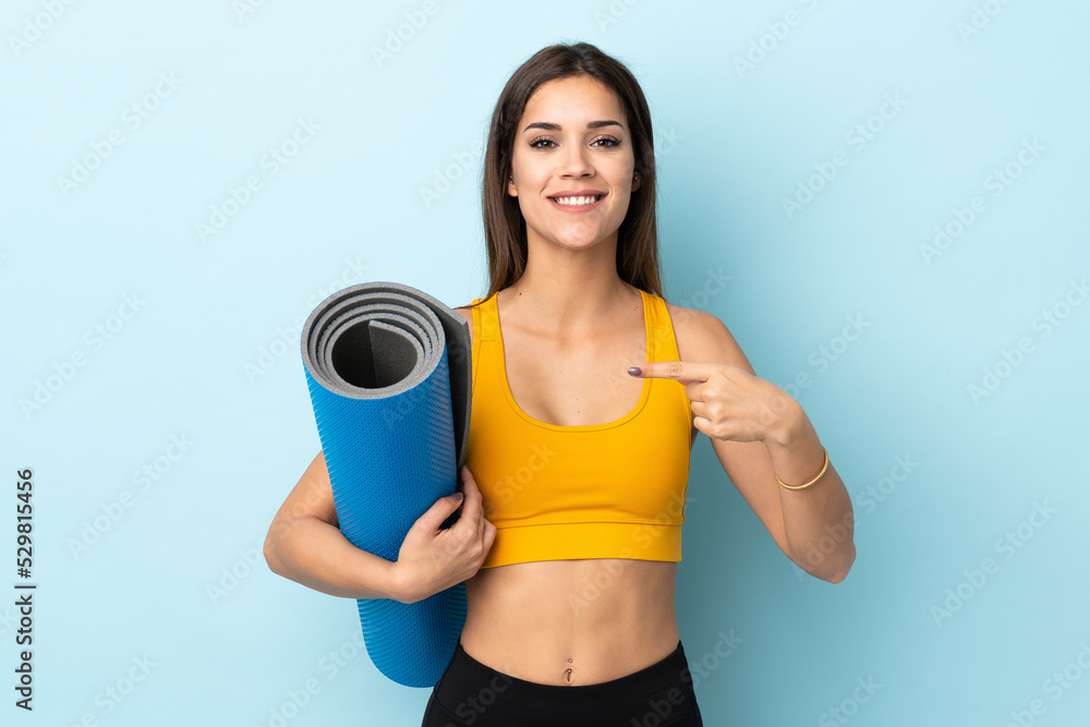Young sport woman with mat isolated on blue background and pointing it Young sport woman with mat isolated on blue background and pointing it