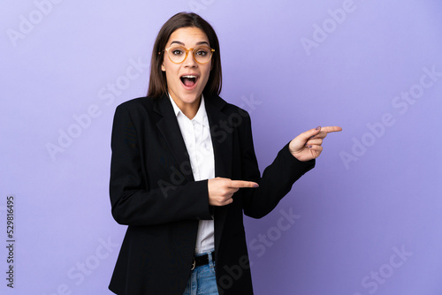 Business woman isolated on purple background surprised and pointing side © luismolinero
