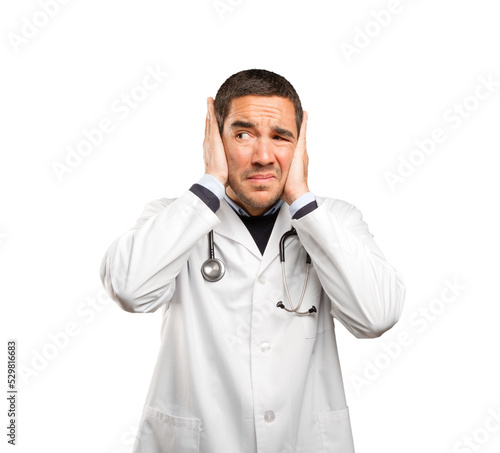 Concerned doctor covering his ears against white background