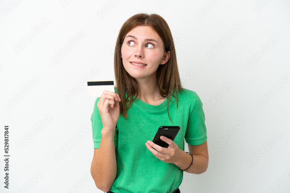 Young English woman isolated on white background buying with the mobile with a credit card while thinking Young English woman isolated on white background buying with the mobile with a credit card while thinking